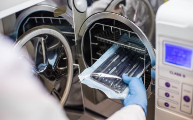 Görüntü, sterilize edilmiş aletleri otomatik klavyenin içine dikkatlice yerleştiren eldivenli bir eli gösteriyor. Hijyen ve ekipman güvenliğinin korunması için önemli laboratuvar protokollerini vurguluyor..