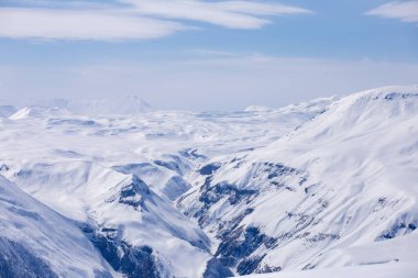 Bu nefes kesen sahnede, el değmemiş beyaz kar, bu karlı dağ manzarasındaki huzur ve güzelliği gösteren, yuvarlanan tepeleri ve keskin tepeleri kaplıyor..