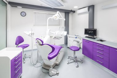 Zarif tasarım elementleri, modern mor ve beyaz mobilyalar, gelişmiş diş ekipmanları ve hasta rahatlığı için yatıştırıcı bir atmosfer içeren şık bir diş kliniği..