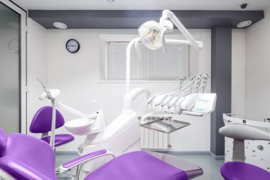 Görüntü, son model ekipman, mor sandalyeler ve ışık dolu bir çevreye sahip sofistike bir diş sağlığı kliniğini gösteriyor. Temizlik ve hasta rahatlığını vurguluyor..