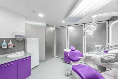 Bu görüntüde, mor dişçi koltuğu, gelişmiş diş teçhizatı ve hasta rahatlığı ve etkili oral bakım için tasarlanmış temiz ve parlak bir atmosferi olan şık, modern bir diş kliniği sergileniyor..