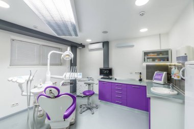 Modern mobilyalar, dişçi koltukları ve diş bakımı için hoş bir ortam sağlamak üzere tasarlanmış özel ekipmanların sergilendiği parlak ve davetkar bir dişçi ofisi..