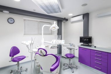 Bu resim modern araçlarla donatılmış şık bir diş kliniği, mor renk düzeni ve hasta rahatlığını ve deneyimini arttırmak için tasarlanmış rahat bir oturma düzenini gösteriyor..