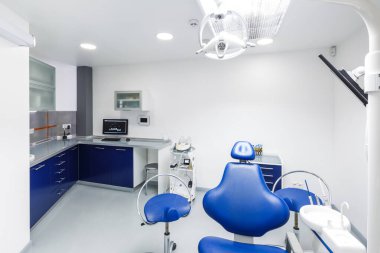 Çağdaş bir diş kliniği, düzenli bir yer, mavi bir diş sandalyesi, gelişmiş aletler ve steril bir ortamda etkin bir hasta tedavisi ve izleme için bir bilgisayar sergiliyor..