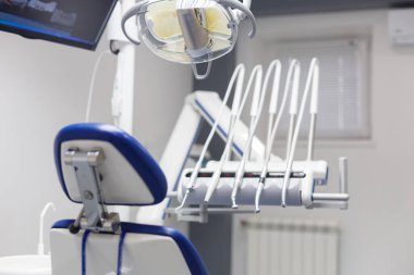 Görüntü, dişçi koltuğu, gelişmiş aletler ve hijyenik ve yüksek teknolojili diş sağlığı ortamını vurgulayan bir monitörün yer aldığı modern bir diş muayenehanesi gösteriyor..