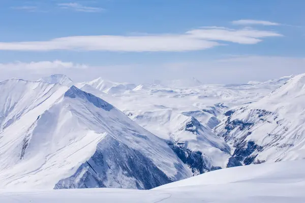 Ufuk boyunca uzanan karla kaplı dağların nefes kesici manzarası dingin mavi bir gökyüzünün altında. Bu kış manzarasının sakinliği doğanın güzelliğini büyülüyor..