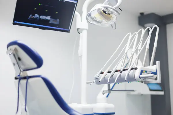 Görüntü, gelişmiş diş aletleriyle donatılmış son model bir diş kliniği, rahat bir hasta koltuğu ve prosedürler için diş görüntülerini gösteren yüksek teknolojili bir monitör gösteriyor..