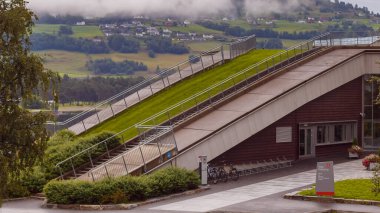 The Voss Kulturhus building features a unique sloping roof with lush green grass, integrating nature into architecture. Surrounded by scenic mountains and charming village life. clipart