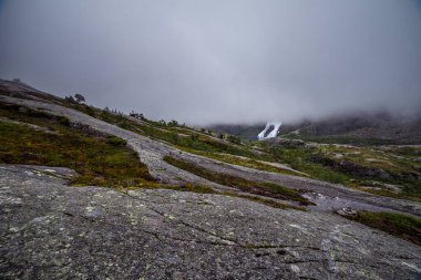 Bu büyüleyici manzara, sisle kaplı dağlık bir alanı yakalar. Kayalık yamaçlar ve yemyeşil ipuçlarını gözler önüne serer. Şelale usulca çağlar ve sakin bir atmosfer yaratır..