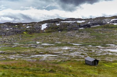 Norveç 'te doğanın güzelliğini gözler önüne seren kayalık tepelerin, yeşil otlakların ve parıldayan su kütlelerinin nefes kesici zeminine yerleştirilmiş ücra bir kulübenin resimsel görüntüsü..