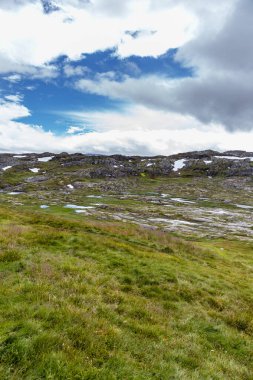 Bu çarpıcı görüntü bereketli yeşillikler, kayalık çıkıntılar ve tüylü bulutlar ve canlı mavi renklerle dolu bir gökyüzü içeren sakin ve dağlık bir manzara sergiliyor. Doğa aşıkları için mükemmel..