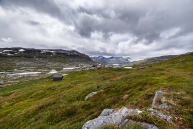Bu nefes kesen manzara, Norveç 'in sakin güzelliğini yakalar. Yeşillik yeşil tepeler, dağınık küçük kulübeler ve bulutlarla kaplı bulutlu bulutlu görkemli dağlar..