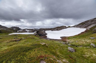 Bu büyüleyici görüntü, kar kalıntıları, canlı yeşil çimenler ve kayalık arazisiyle çok güzel bir dağ manzarası sergiliyor. Açık hava maceralarına ilham veren doğa elementlerinin uyumlu bir karışımı..