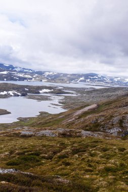 Bu görüntü, sakin göller, yuvarlanan tepeler ve çarpıcı bulutlu gökyüzünün altında doğanın harikalarını gösteren görkemli dağların yer aldığı nefes kesici bir dağ manzarası yakalar..