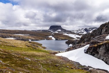 Bu çarpıcı görüntü engebeli, karla kaplı dağlar ve yeşil tepelerle çevrili sakin bir gölü yakalar. Bu da onu doğa maceraları ve doğa meraklıları için mükemmel bir yer yapar..