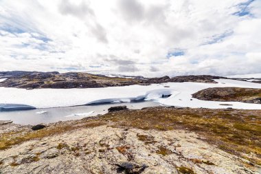 Bu nefes kesici görüntü, kar, kaya ve bulutlarla çevrili sakin bir buzul gölü barındıran Kuzey Kutbu manzarasının güzelliğini gözler önüne seriyor..