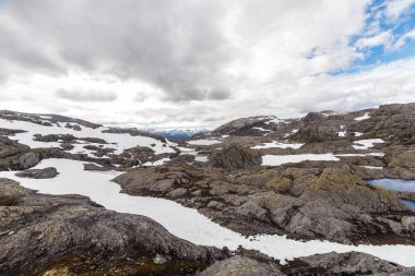 Bu resim, üzerinde geniş bir gökyüzü bulunan kayalık oluşumlar ve karla kaplı alanların bir karışımını gösteren nefes kesici bir manzara yakalar. Doğal güzelliğin gerçek bir tasviri..
