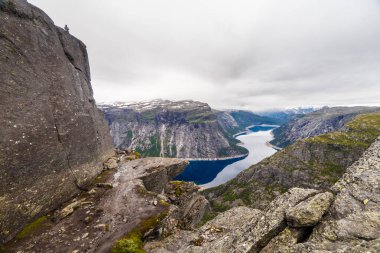 Bu büyüleyici görüntü, bir uçurumun kenarından hayranlık uyandırıcı bir görüntü yakalar. Derin mavi fiyort, dramatik dağlar ve bulutlu bir gökyüzü sergiler. Norveç 'in tüm güzelliklerini gözler önüne serer..