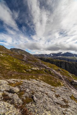 Büyüleyici bulutlu gökyüzünün altında yemyeşil ve kayalık arazi içeren geniş bir dağ manzarası maceraperest yürüyüşçülerin vahşi doğanın doğal güzelliklerini keşfettiği yer..