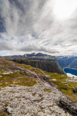 Geniş bir engebeli dağ arazisi manzarası çimen parçalarıyla süslenmiş, bulutlarla dolu karmaşık bir gökyüzü altında, Norveç 'in altındaki el değmemiş fiyortları sersemletici doğayı ortaya çıkarıyor..