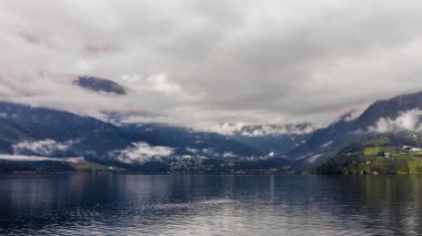 Bu çarpıcı görüntü Norveç fiyortunun sakin güzelliğini yakalar. Sisli dağları, durgun suları ve dingin yeşil tepeleri, dingin atmosferi yansıtır..