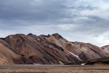 Engebeli bir dağ silsilesinin çarpıcı bir görüntüsü zengin renkler ve dokular sergiliyor, dramatik bir gökyüzü ile kaplanıyor, hayranlık uyandıran, güzelliklerle dolu doğal bir manzara yaratıyor..