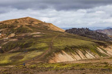 İzlanda 'nın nefes kesici doğal güzelliğini keşfedin, canlı dağ yamaçları, dolambaçlı yollar, ve gizemli, bulutlarla dolu bir gökyüzünün ortasında maceraperest yürüyüşçüler..