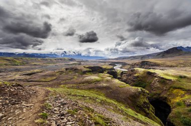 Bu çarpıcı görüntü İzlanda 'nın engin ve engebeli manzarasını gözler önüne seriyor, dramatik bulut oluşumları, yeşil tepeler ve bu resim gibi doğal ortamda dolanan bir nehir..