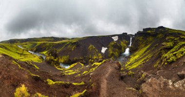 Bu nefes kesen manzara İzlanda 'nın büyüleyici manzaralarını sergiliyor. Canlı yeşil tepeler, akan nehirler ve kasvetli, bulutlu bir atmosferin ortasında güzel bir şelale..