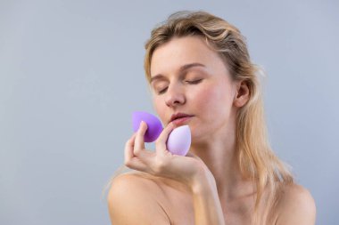 Bu resim, makyaj uygulaması sanatını vurgularken zarif makyaj süngerleri tutan, zarafet ve yumuşaklık sergileyen bir kadını güzel bir şekilde yakalıyor..