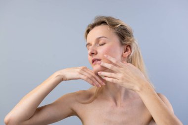 Nazik bir ifadeyle bir kadını gösteren sakin bir görüntü, gözleri kapalı, sükuneti yansıtan, narin elleri yüzünde dinlenirken, iç gözlem ve huzuru anımsatan bir an..