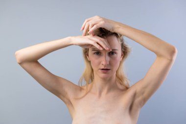 Görüntü uzun saçlı bir modeli gösteriyor, düşünceli bir yansımayla meşgul, elleri zarif bir şekilde başının ve alnının üzerine yerleştirilmiş, tarafsız bir zemine karşı..