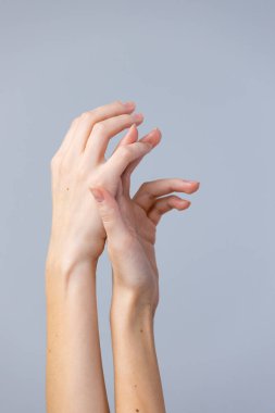 Görüntü, zarif bir şekilde birbirine dolanmış iki eli, zarif bir şekilde uzanan ve dokunan parmaklarıyla, yumuşak, nötr bir arkaplana vurguluyor, narin formlarını ve güzelliklerini vurguluyor..