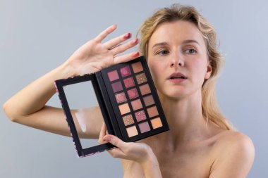 Çağdaş moda ve kozmetik tasarımlarla güzellik eğilimlerini ve sanatını vurgulayan, çeşitli tonlarla dolu canlı bir makyaj paletini zarif bir şekilde tutan bir modelin çarpıcı görüntüsü..