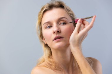 Bu resimde, bir kadın titizlikle göz kalemi kullanmaya odaklanır, güzellik rutinlerinin özünü yakalar ve makyaj uygulama geliştirme sanatını gözler önüne serer..