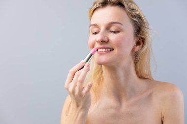 Bu çarpıcı görüntüde, güzel genç bir kadın neşeyle pembe ruj sürüyor. Onun doğal parıltısı ve ışıl ışıl gülüşü güzellik bakımında bir neşe ve kişisel stili yansıtır..