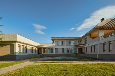 Bu resim, geniş pencereli ve yemyeşil çimenli güzel tasarlanmış modern bir bina sergiliyor. İnsanları mimari zarafetini ve huzurlu çevresini takdir etmeye çağırıyor..