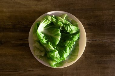 Beyaz bir tabakta taze yeşil marul yapraklarından oluşan canlı bir düzenleme, kırsal ahşap bir arka plana dayanıyor. Salata, garnitür ya da sağlıklı tarifler için idealdir..