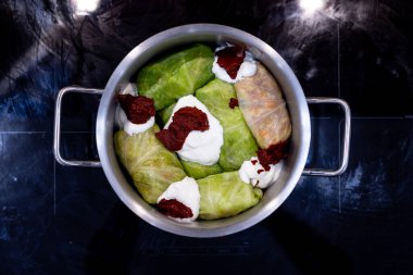 Lezzetli bir dolma ile dolu canlı bir üzüm yaprakları gösterisi, kremalı sos ve baharatlı macunla süslenmiş, hepsi de baştan çıkarıcı bir mutfak sahnesini gösteren bir tencereye yerleştirilmiş..