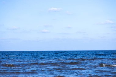 Bu resim okyanusun çarpıcı bir görüntüsünü sergiliyor. Derin mavi su yavaşça kıyıya vuruyor. Gökyüzü parlak ve berrak. Yumuşak bulutlarla noktalanmış. Huzurlu bir sahil manzarası yaratıyor..