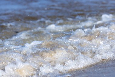 Bu resim, su ve kumların hoş etkileşimlerini gösteriyor, nazik dalgalar yavaşça çarpıyor, kabarcıklar ve sakin sahil güzellikleriyle dolu büyüleyici bir sahne yaratıyor..