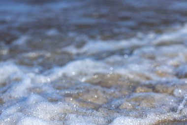 Okyanus dalgalarının karmaşık detaylarını gösteren büyüleyici bir görüntü. Güneş ışığı köpüğü yakalıyor ve şaşırtıcı bir ışıltı yaratıyor. Huzurlu kıyı atmosferini güçlendiriyor..