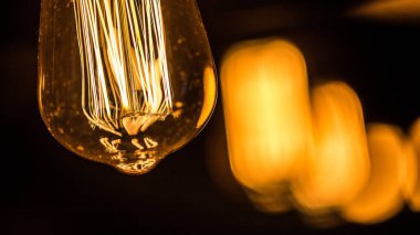 Bu resimde, çarpıcı lifleri olan güzel aydınlatılmış bir Edison ampulü var. Sıcak ışıltı, karanlık arkaplana zıt düşerek modern iç dekora cazibe ve zarafet katıyor..