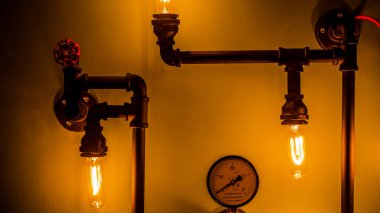 Bu resim, borulardan, klasik ampullerden ve dekoratif kapakçıktan yapılmış büyüleyici bir endüstriyel duvar ışığı sergiliyor. Herhangi bir yerde rahat bir atmosfer yaratmak için mükemmel..