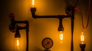 Görüntü, siyah metal borulara yerleştirilmiş klasik Edison ampullerini içeren endüstriyel tarzda ışıklandırma sergiliyor, bir gösterge ve kırmızı kapakçık ile tamamlanmış, samimi bir ortam yaratıyor..