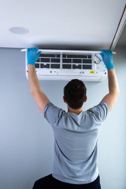 Görüntü, bir teknisyenin evdeki iklim kontrol sistemleri üzerinde çalışırken profesyonellik ve güvenlik sergileyerek bir klima ünitesini korumaya odaklandığını gösteriyor..