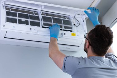 Bir teknisyen bir havalandırma ünitesine hizmet vermekle meşgul, temizleme filtrelerine ulaşmak için dikkatlice kapağı kaldırıyor, modern ortamlarda gerekli HVAC bakım becerilerini gösteriyor.
