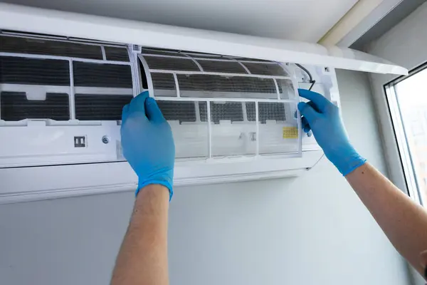 Mavi eldiven giyen bir bireyin yakından çekimi, özenle havalandırma ünitesinden hava filtresini çıkarıyor. Bu, soğutma sistemleri için düzenli bakımın önemini gösterir.