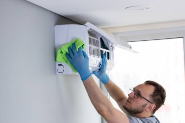 Mavi eldivenli yetenekli bir teknisyen, ev içi havalandırma ünitesini titizlikle temizliyor, temizliği arttırmak ve ev konforu için daha iyi hava kalitesini sağlamak için yeşil bir bez kullanıyor..