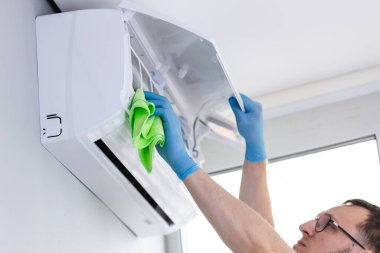 Klimayı kumaşla dikkatlice temizleyen bir birey, kapalı hava kalitesi ve sistem verimliliği açısından düzenli bakımın önemini vurgularken görülüyor..